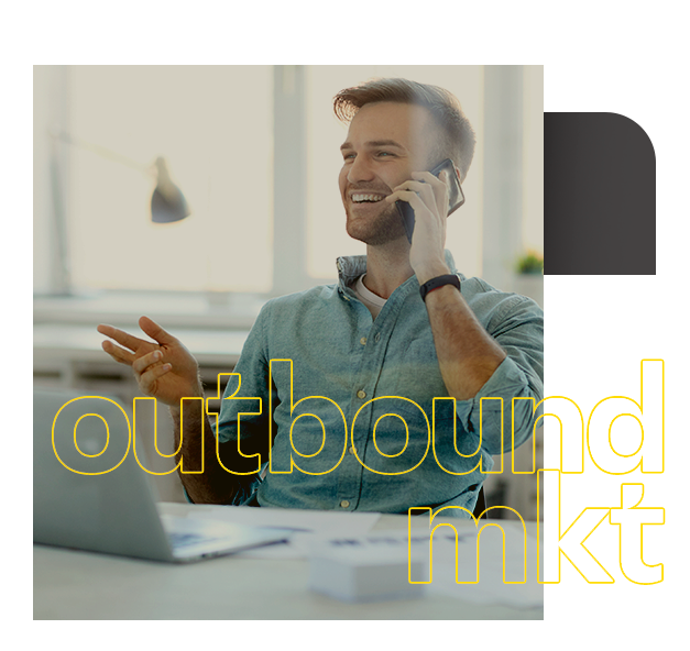 Um homem está sentado em uma mesa falando ao celular. Outbound