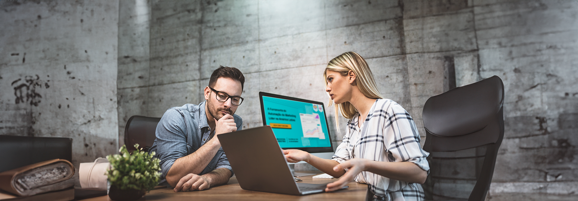 Um homem e uma mulher estão sentados à mesa olhando para um laptop.