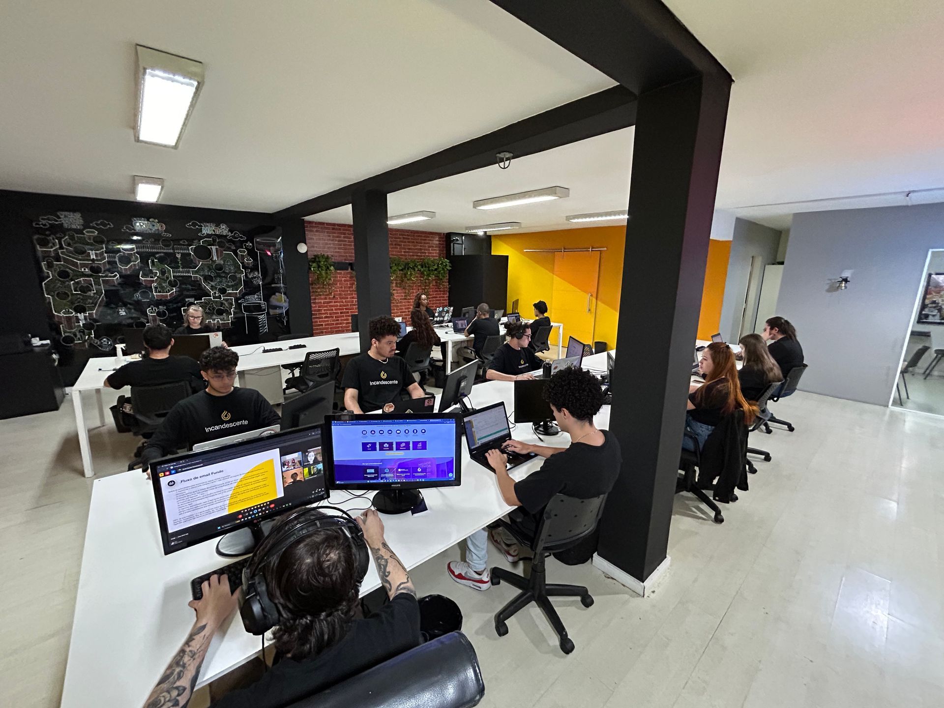 Um grupo de pessoas está sentado em mesas em um escritório trabalhando em computadores.